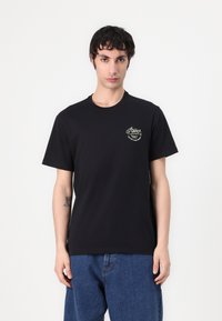 Black cotton t-shirt featuring a front chest logo in gold with curved text. The fit is standard, sleeves are short, and the fabric is smooth.