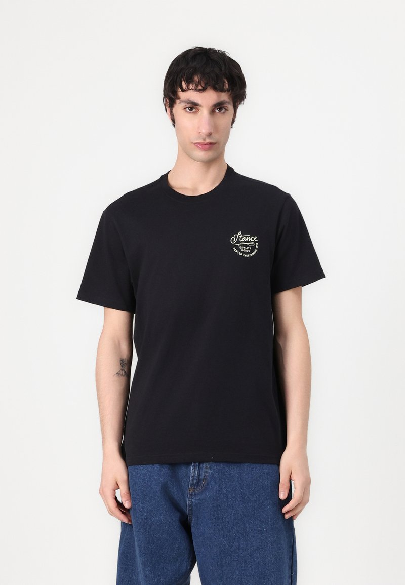 Black cotton t-shirt featuring a front chest logo in gold with curved text. The fit is standard, sleeves are short, and the fabric is smooth.
