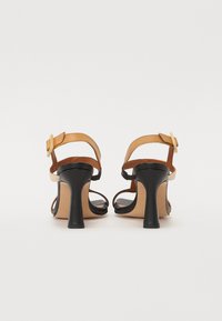 Sorte og brune hæle sandaler med en strappy design, en solid sort hæl og justerbare ankelstropper med guldfarvede spænder.