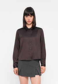 Chemise boutonnée en satin brun foncé avec un col et des manches longues, associée à une jupe grise avec deux fentes avant.