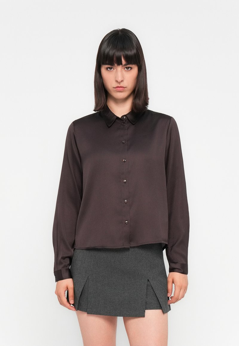 Chemise boutonnée en satin brun foncé avec un col et des manches longues, associée à une jupe grise avec deux fentes avant.