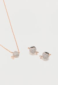 Κολιέ από ροζ χρυσό και αντίστοιχα σκουλαρίκια καρφωτά με μενταγιόν σε σχήμα καρδιάς, διακοσμημένα με μικρούς διάφανους κρυστάλλους σε λευκό φόντο.