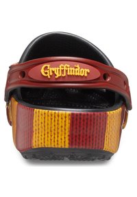 Zuecos temáticos de Gryffindor con diseño a rayas rojas y amarillas, parte superior texturizada, suela negra y logotipo en relieve prominente en una correa color marrón.