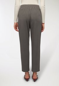 Szare spodnie z elastycznym pasem o luźnym kroju, charakteryzujące się gładką fakturą i zwężanymi nogawkami, w połączeniu z czerwonymi sandałami na obcasie.