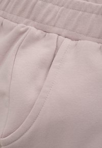 Lichtroze sweatpants met een geribbelde tailleband, zijzakken en een zachte textuur. Heeft een gedrapeerd stofdetail nabij de tailleband.