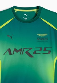 Zielona sportowa koszulka z krótkim rękawem o gradientowym wzorze, z czarnym napisem "AMR25", logo Pumy oraz brandingiem Aston Martin w żółtych akcentach.
