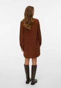 Robe marron à manches longues avec une coupe décontractée, dotée d'un col rond et de boutons décoratifs sur les poignets, associée à des bottes marron montantes.