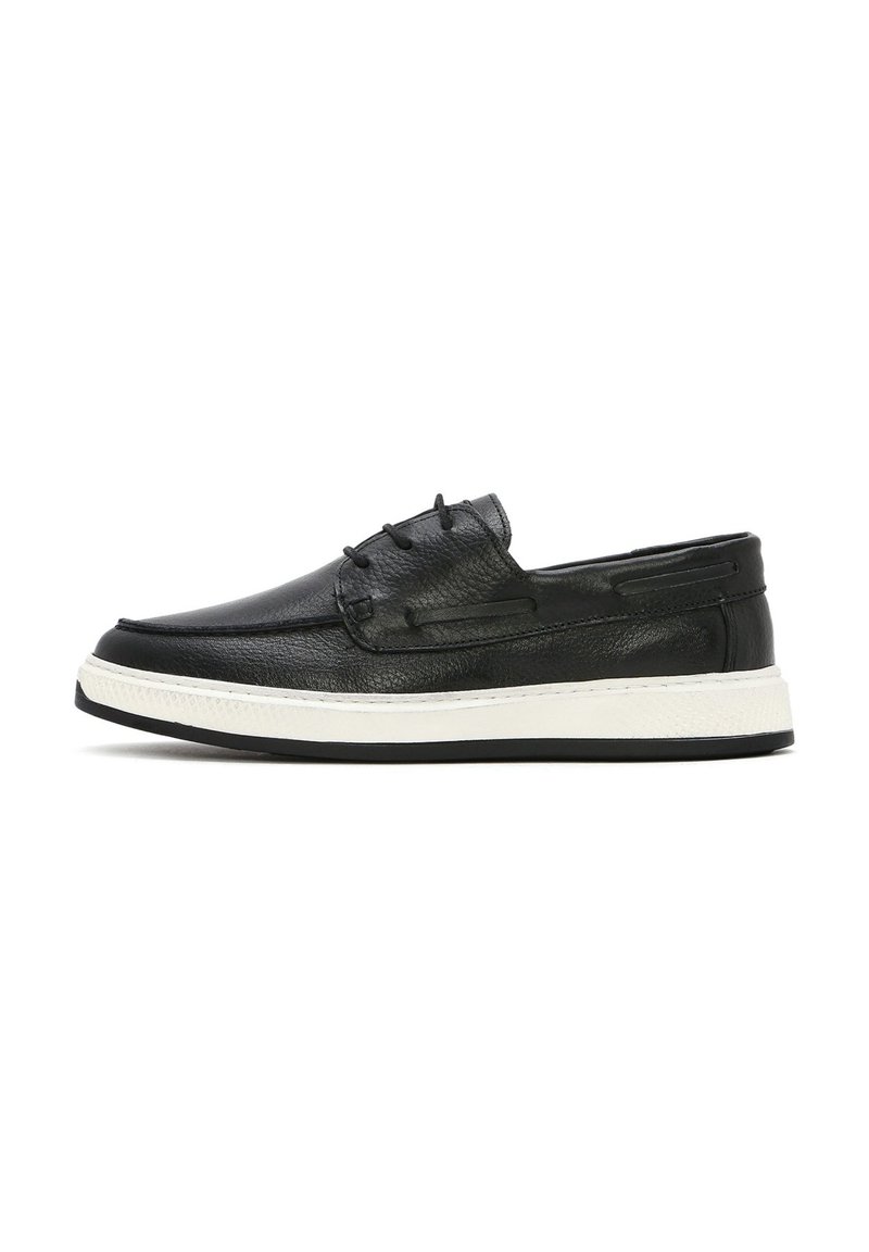 Scarpa slip-on in pelle nera con superficie testurizzata, dotata di suola in gomma bianca e dettagli di cucitura sottili per un tocco aggiuntivo.