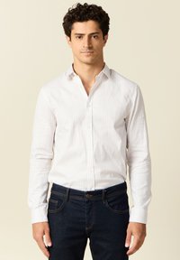Weißes Hemd mit blauen vertikalen Streifen, langen Ärmeln und Kragen, kombiniert mit dunklen blauen Jeans. Schlichtes Design mit klassischen Merkmalen.