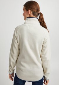 Krēmkrāsas vilnas džemperis ar augstu apkakli, viegli izliekts apakšmala un kontrastējoši zili akcenti uz apkakles un aprocēm. Mīksta, teksturēta auduma.