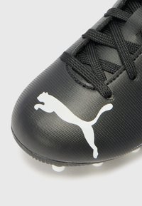 Musta jalkapallokenkä, jossa on teksturoitu pinta, mustat nauhat ja valkoinen Puma-logo. Varustettu valkoisilla napeilla pohjassa.