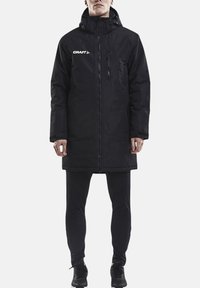 Schwarze isolierte Jacke mit hohem Kragen, durchgehendem Reißverschluss und Reißverschlusstasche auf der Brust; mit dem "CRAFT"-Logo in Weiß.