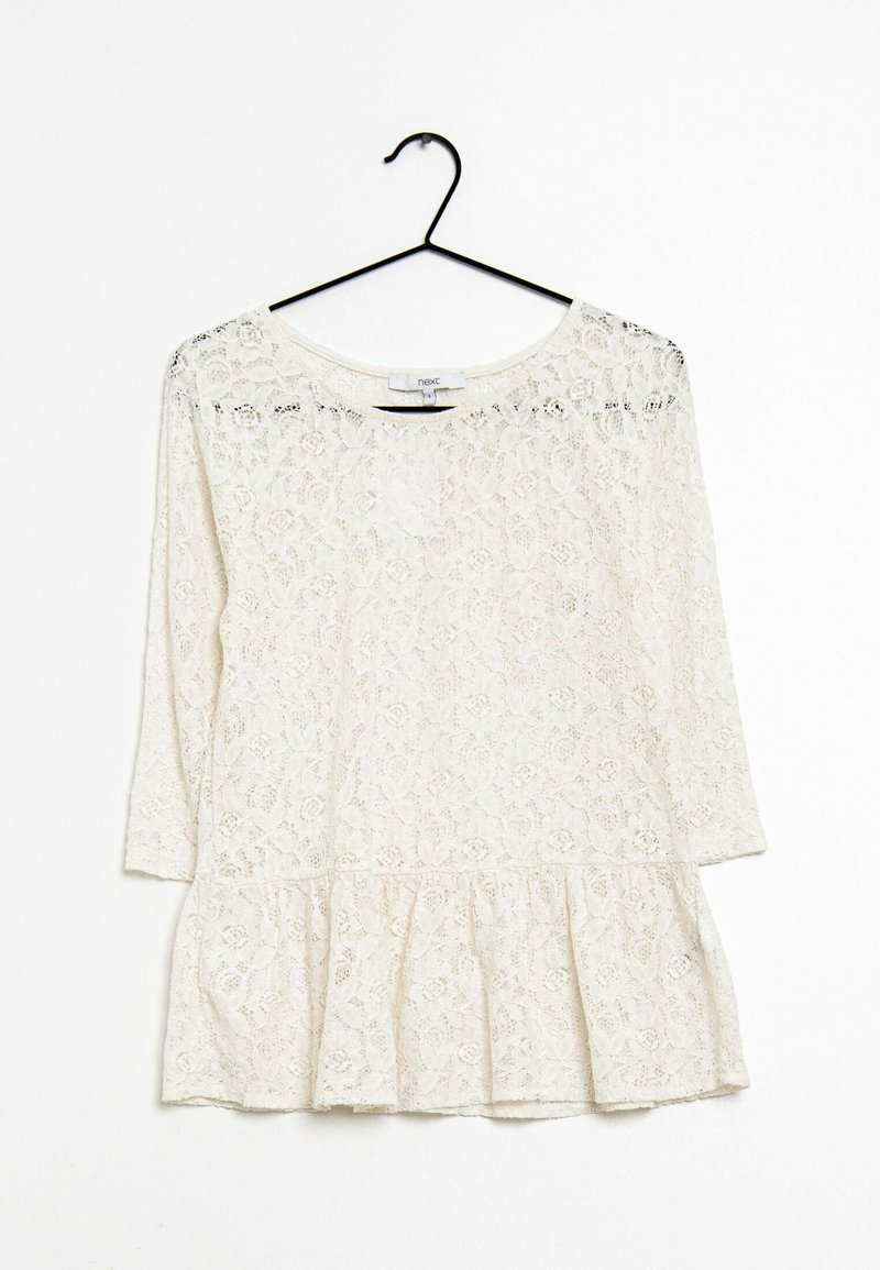 Haut en dentelle blanc cassé avec des manches trois-quarts, un col rond et un ourlet en peplum. Arbore des motifs floraux tout au long.