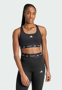 Svart sports-bh med justerbare stropper, med hvit Adidas-logo. Kombinert med svarte Techfit leggings, begge laget av glatt, elastisk stoff.