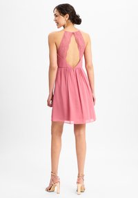 Rosa Halterkleid mit Spitzenrücken, fließendem Stoff und ausgestelltem Rock. Es hat einen tiefen Rückenausschnitt und eine weiche Textur.
