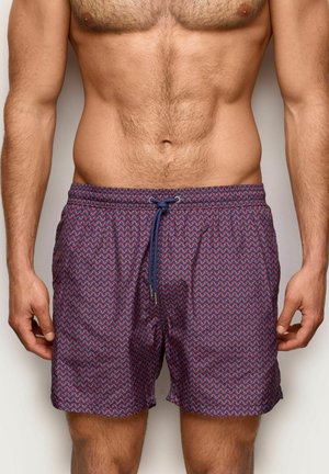 Homme portant un short de bain rouge foncé avec un petit motif répétitif de vagues multicolores et un cordon de serrage bleu marine.