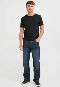 Camiseta de algodón negra combinada con vaqueros azul oscuro de pierna recta y una costura sutil, llevada con unas zapatillas negras de corte bajo.