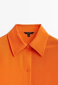 Orange collared shirt with a smooth texture, featuring a front button closure and a label on the inside neck area.