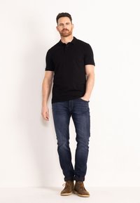 Černé polo tričko s krátkým rukávem a třemi knoflíky, kombinované s úzkými tmavě modrými džínami a hnědými semišovými kotníkovými botami.