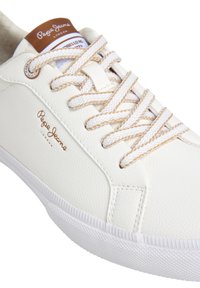 Weißer Sneaker aus strukturiertem Kunstleder mit beigen Schnürsenkeln und Akzenten. Verfügt über ein braunes Logo-Label an der Zunge. Flache Gummisohle.