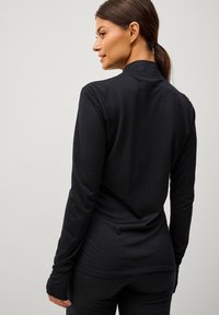 Zwarte top met lange mouwen, gemaakt van zacht materiaal, met een aansluitend ontwerp en hoge kraag. Heeft duimgaten bij de manchetten voor extra bedekking.