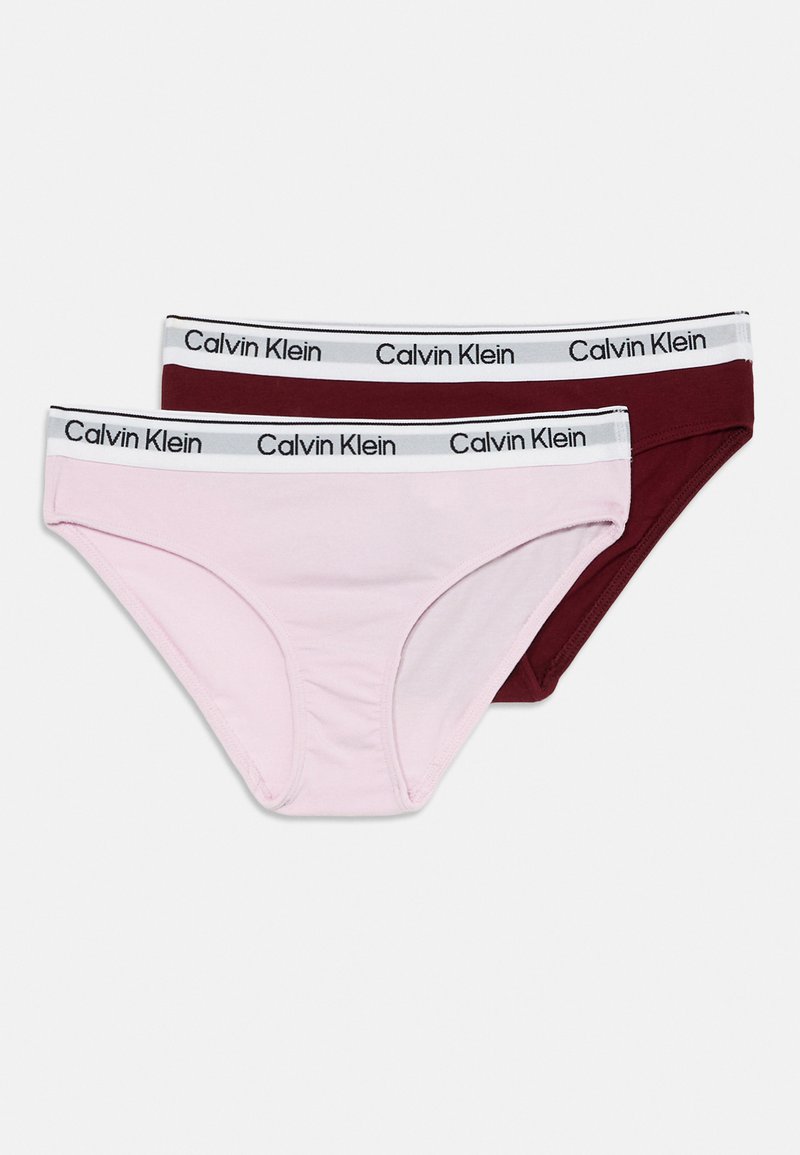 Dva páry bavlnených nohavičiek v ružovej a tmavočervenej farbe. Každé má biely pásik s čiernym logom "Calvin Klein".