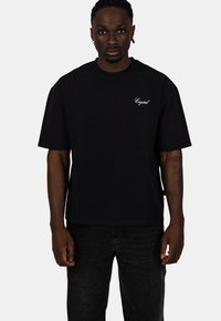 Czarna bawełniana koszulka z krótkim rękawem, z białym haftem "Crystal" na piersi, w połączeniu z ciemnoniebieskimi dżinsami.