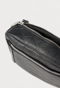 Czarna skórzana torba z pikowaną fakturą, wyposażona w srebrny zamek błyskawiczny i zwartą formę. Powierzchnia zdobiona jest wzorem diamentowym.