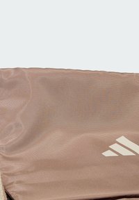 Saco de desporto rosa claro com um tecido texturizado e acabamento brilhante, embelezado com um logo de três riscas brancas na lateral.