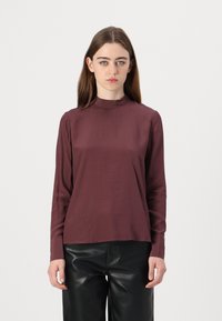 Long-sleeve top in burgundy, featuring a high neckline and smooth texture. Paired with high-waisted black pants for contrast.