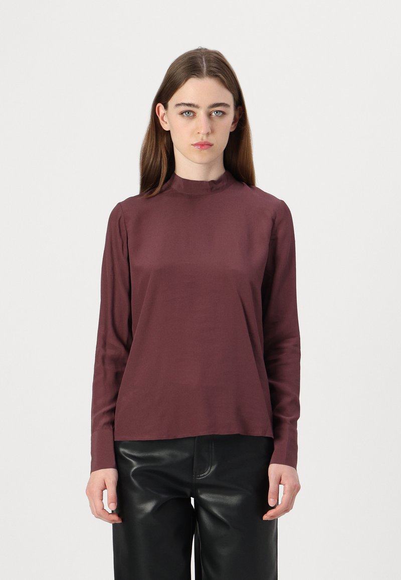 Long-sleeve top in burgundy, featuring a high neckline and smooth texture. Paired with high-waisted black pants for contrast.