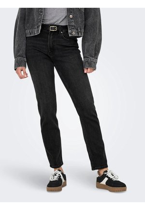 Person trägt schwarze High-Waist-Jeans, schwarzen Gürtel mit goldener Schnalle, schwarze Jeansjacke, weißes Top und schwarze Sneaker mit weißen Schnürsenkeln und braunen Sohlen.