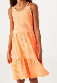 Vestido de color durazno hecho de tela texturizada, con diseño sin mangas, parte superior acanalada y falda en capas. Acentuado con tirantes delgados.