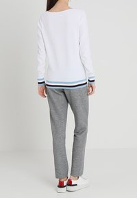 Witte top met lange mouwen en een geruite zoom in blauw en bruin, gecombineerd met grijze joggingbroek en witte sneakers met rode accenten.