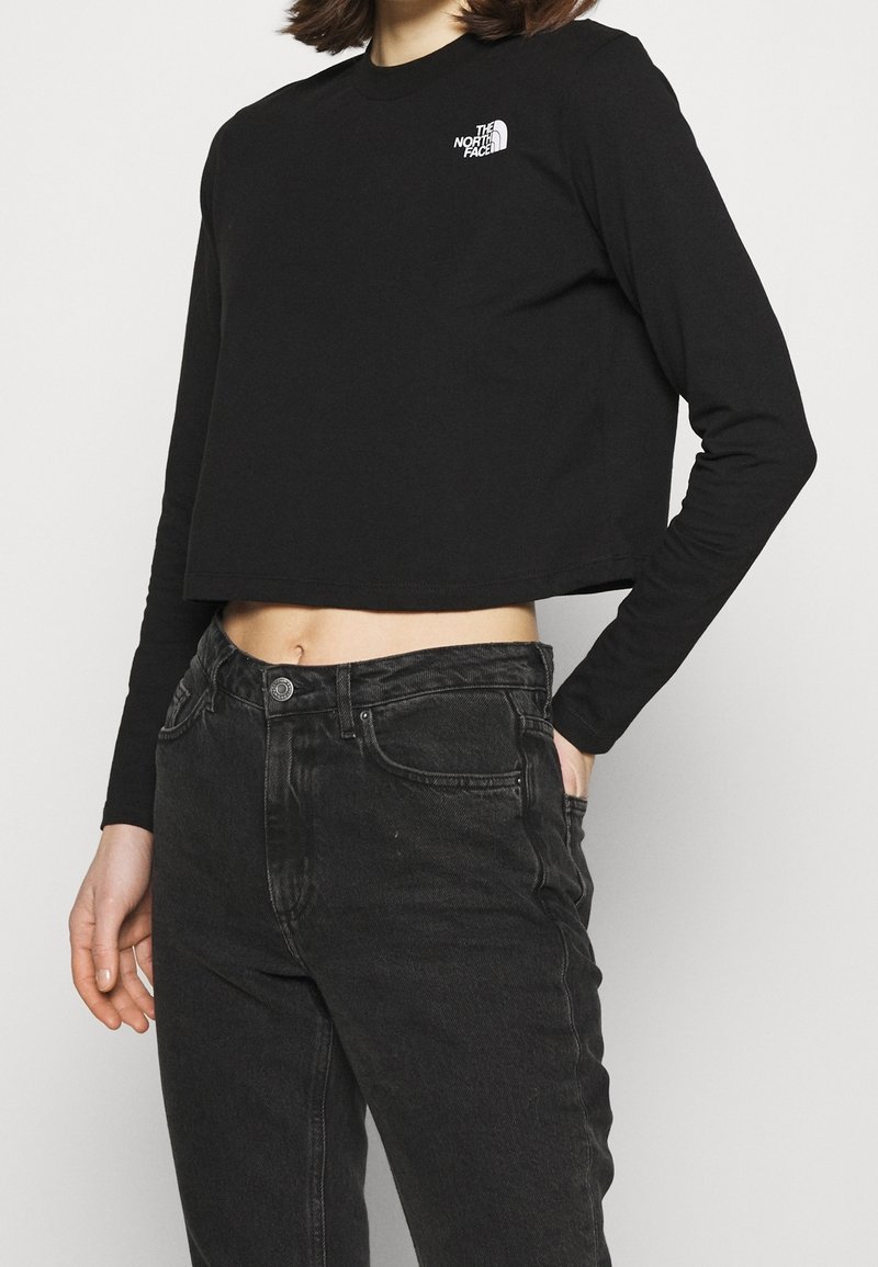 Svart kortärmad långärmad skjorta med rund halsringning och en vit logotyp på bröstet, i kombination med högmidjade svarta jeans.