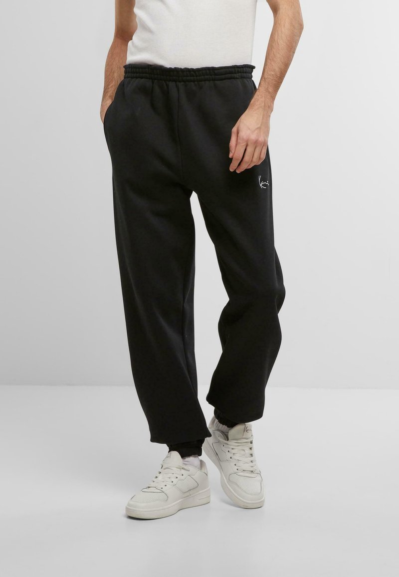 Pantalon de survêtement noir avec une taille élastique, des poches latérales et un petit logo blanc à l'avant. Matière en coton mélangé lisse.