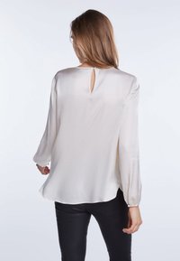 Blusa di seta in crema chiaro, caratterizzata da maniche lunghe con polsini aderenti e un dettaglio a chiave sul retro. Texture liscia con una vestibilità comoda.