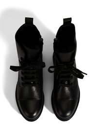 Ein Paar schwarze Lederstiefeletten mit Schnürsenkeln, von oben auf einem weißen Hintergrund betrachtet.