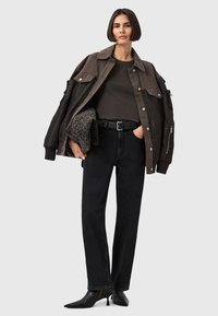 Giacca marrone oversize con ampie tasche sopra una maglietta scura, abbinata a jeans neri a gamba dritta e tacchi neri a punta.