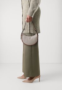 Kulatá kabelka s tkaným vzorem v béžových a hnědých odstínech, s tmavými koženými detaily a ramenním popruhem. Nositelná s širokými kalhotami a podpatky.