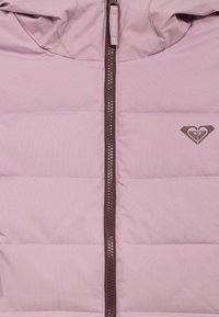 Lys rosa dunjakke med glidelås foran og hette. Har vertikale quiltede paneler og en mørk rosa hjerte-logo på venstre bryst.