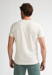 Camiseta de manga corta color beige claro con un patrón texturizado de sutiles motas de colores. Cuello redondo, tela suave y diseño ajustado.