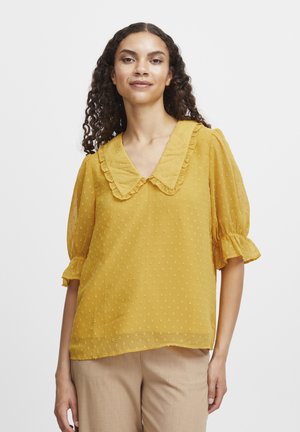 Sennepsgul bluse med en flæsekrave og korte, puffede ærmer. Den strukturerede stof har små, hævede prikker. Let og luftigt design.
