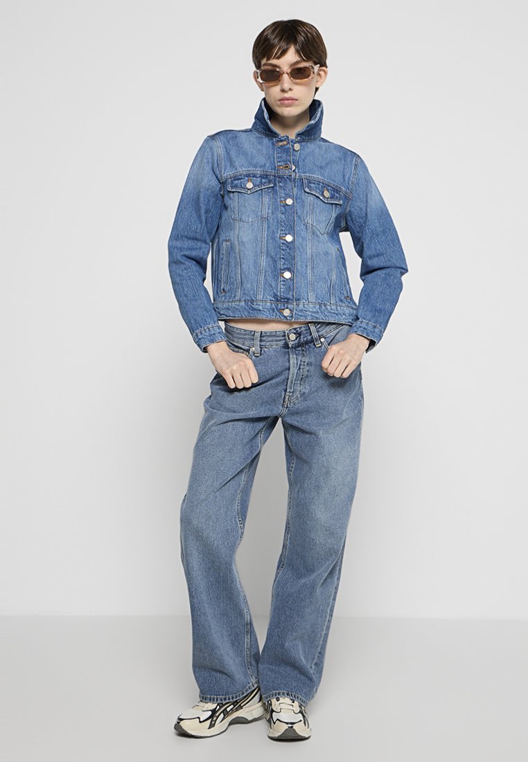 Blaues Denim-Jacket mit verkürztem Schnitt, Brusttaschen und Knopfverschluss, kombiniert mit lässigen blauen Denim-Jeans und sportlichen Schuhen.