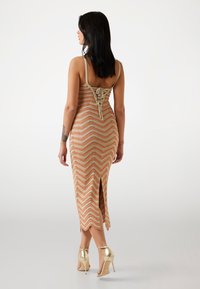 Lekka, dzianinowa sukienka w jodełkę z odkrytymi plecami, rozcięciem u dołu i cienkimi ramiączkami. Noszona z błyszczącymi, złotymi szpilkami.