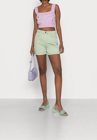 Světle fialový pletený crop top se čtvercovým výstřihem, zelené džínové šortky, levandulová kabelka a zelené sandály na podpatku s pleteným designem.
