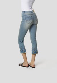 Lichtblauwe denim capri-jeans met decoratieve patronen in blauw en goud aan de zoom, met een rafelige rand en standaard achterzakken.