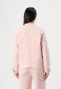 Chaqueta de mezclilla rosa que presenta un diseño clásico, puños con botones y detalles de costura en la parte posterior. El material tiene un acabado ligeramente desteñido.