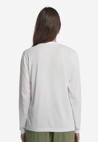Weißes Langarmshirt aus weichem Baumwollstoff. Mit Rundhalsausschnitt und gerippten Bündchen. Schlichtes Design ohne Muster oder Akzente.