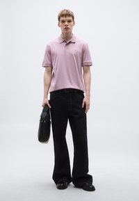 Roza polos majica, temne denim široke hlače, črni usnjeni čevlji in črna torbica. Gladek material, sproščen kroj, minimalistični oblikovalski detajli.